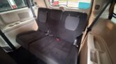 Back row of a beige vehicle with three black fabric seats and visible seat belts (interior shot).