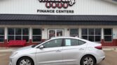 Silver sedan parked in front of a Wheel City Auto Finance Centers storefront, with a window sticker visible on the passenger door.