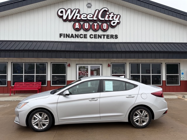 Silver sedan parked in front of a Wheel City Auto Finance Centers storefront, with a window sticker visible on the passenger door.