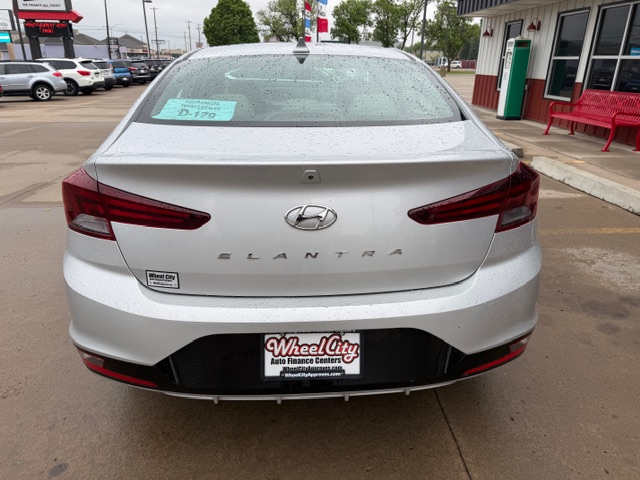 Rear view of a silver Hyundai Elantra in a dealership lot on a rainy day, showing the ELANTRA badge and dealership license plate frame.
