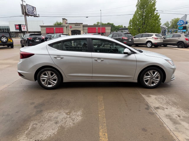 Side view of a silver four-door sedan parked in a parking lot beside a row of shops.