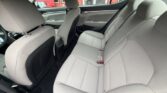 Interior of a light gray sedan showing the rear seats and front seats from the open rear door, fabric upholstery and seat belts visible