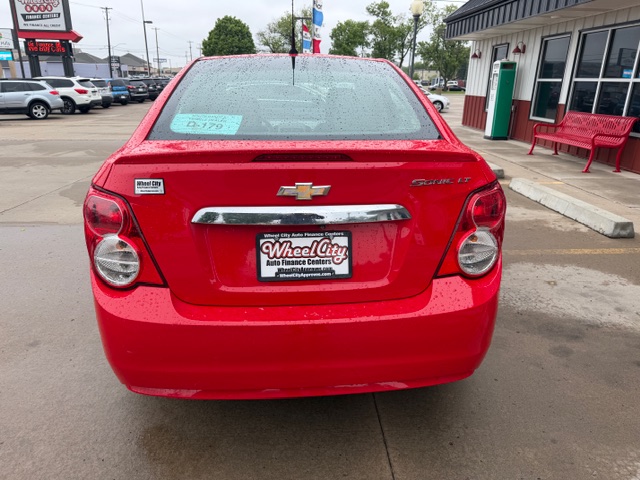 Rear view of a red Chevrolet car with Wheel City license plate frame in a dealership lot. Rain on the rear window and taillights visible.