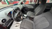 Interior of a Chevrolet car with gray fabric seats, showing the steering wheel, dashboard, center console, and automatic gear shifter; floor mat visible on the driver's side.