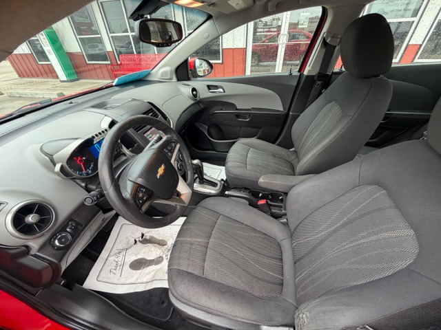 Interior of a Chevrolet car with gray fabric seats, showing the steering wheel, dashboard, center console, and automatic gear shifter; floor mat visible on the driver's side.