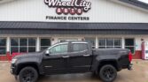 Black four-door pickup truck parked in front of Wheel City Auto Finance Centers storefront.