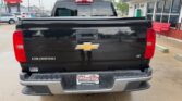 Rear view of a black Chevrolet Colorado LT pickup truck in a dealership lot, displaying the gold bowtie emblem and 'Colorado LT' on the tailgate.