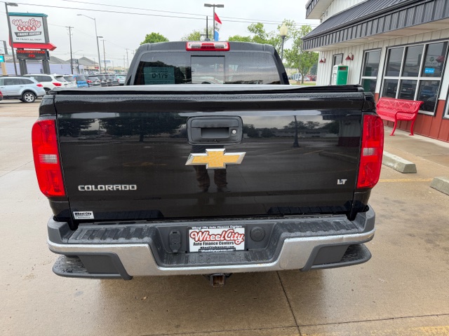 Rear view of a black Chevrolet Colorado LT pickup truck in a dealership lot, displaying the gold bowtie emblem and 'Colorado LT' on the tailgate.