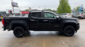 Black crew-cab Chevrolet Silverado pickup truck parked in a parking lot, side view with black wheels and tinted windows.