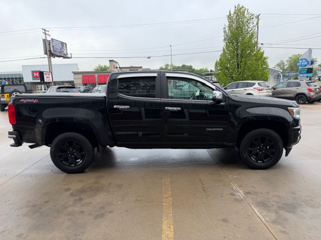 Black crew-cab Chevrolet Silverado pickup truck parked in a parking lot, side view with black wheels and tinted windows.