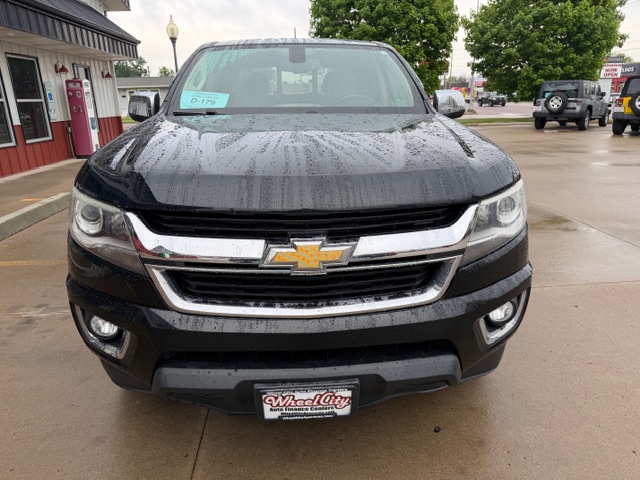 Front view of a black Chevrolet pickup truck parked in a dealership lot on a rainy day, showing the chrome grille, gold bowtie emblem, and Wheel City plate.