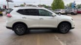 White crossover SUV photographed from the side in a car lot, with other vehicles and dealership buildings in the background.