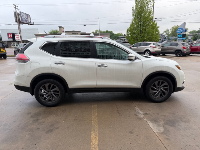 White crossover SUV photographed from the side in a car lot, with other vehicles and dealership buildings in the background.