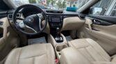 Front interior of a beige Nissan with steering wheel, dashboard, center console, and tan seats.
