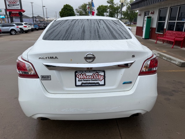 Rear view of a white Nissan Altima S in a dealership lot, raindrops on the rear window; dealer plate reads Wheel City Auto Finance Centers.