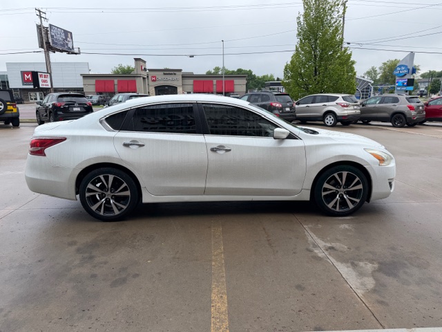 White four-door sedan in a dealership lot, side view with dark tinted windows and black alloy wheels, parked among other cars
