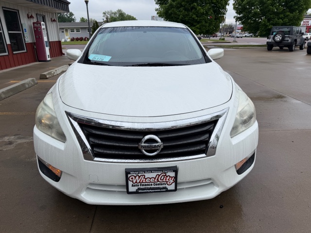 Front view of a white Nissan sedan parked in a dealership lot, with a Wheel City Auto Finance Centers license plate frame on the bumper.