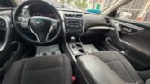 Interior of a car cabin: front seats, steering wheel, center console, and gear shifter visible from the driver’s seat (Nissan).