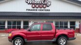 Red four-door pickup truck parked in front of Wheel City Auto Finance Centers storefront, dealership signage visible above.