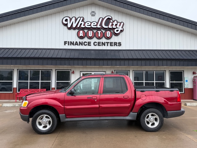 Red four-door pickup truck parked in front of Wheel City Auto Finance Centers storefront, dealership signage visible above.