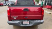 Rear view of a red Ford Explorer pickup with the tailgate up, chrome bumper, and a dealership license plate frame on a wet parking lot surface.