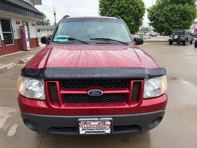 Front view of a red Ford SUV parked in a dealership lot on a rainy day, with a black hood deflector and a Wheel City Auto Finance Centers plate.
