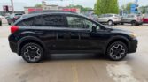 Side view of a black compact SUV with tinted windows and stylish alloy wheels parked in a car lot with other vehicles and storefronts in the background.