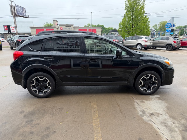 Side view of a black compact SUV with tinted windows and stylish alloy wheels parked in a car lot with other vehicles and storefronts in the background.