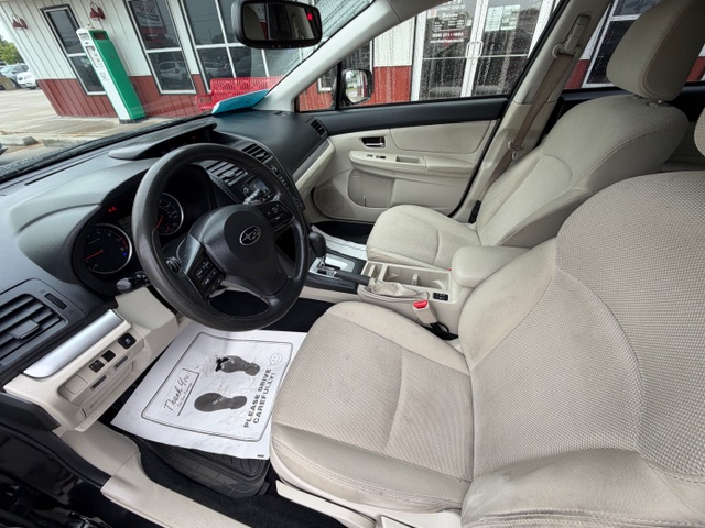 Front interior of a beige SUV showing steering wheel, driver and passenger seats, center console, and a dealership exterior visible through the windows.
