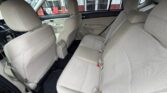 Light beige fabric interior of a sedan shown from the rear passenger side, front seats visible, spacious back bench with three seat belts and doors open.