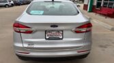 Rear view of a silver Ford sedan parked in a car dealership lot, with a Wheel City Auto Finance Centers license plate frame visible on the trunk.