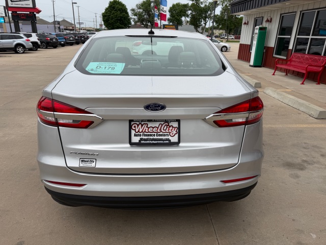 Rear view of a silver Ford sedan parked in a car dealership lot, with a Wheel City Auto Finance Centers license plate frame visible on the trunk.