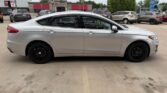 Side view of a silver four-door sedan with black wheels parked in a car lot outside a dealership.