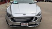 Front view of a silver Ford sedan parked at a dealership, showing grille and headlights.