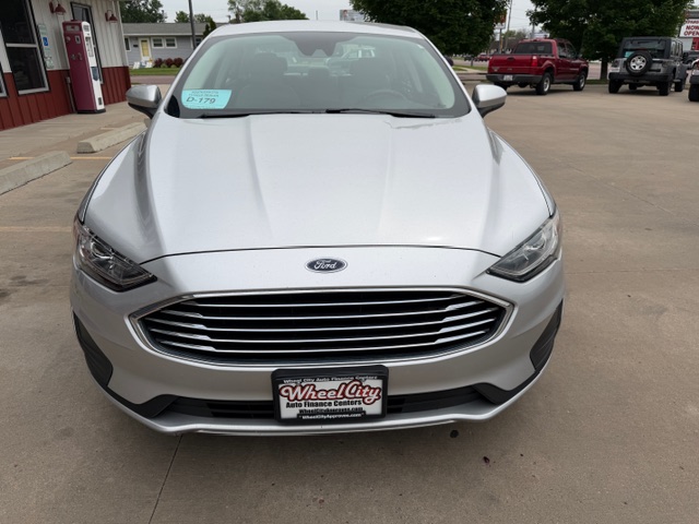 Front view of a silver Ford sedan parked at a dealership, showing grille and headlights.
