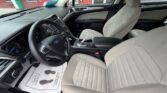 Front interior of a Ford SUV with beige fabric seats, black dashboard, and steering wheel; driver’s seat shows controls and center console; paper floor mat with footprints on the driver side.