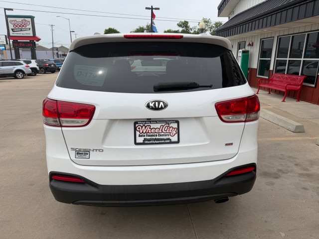 White Kia SUV rear view at a car dealership, with a Wheel City license plate frame visible on a cloudy day.