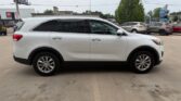 Side view of a white SUV parked in a car dealership lot with other vehicles in the background.