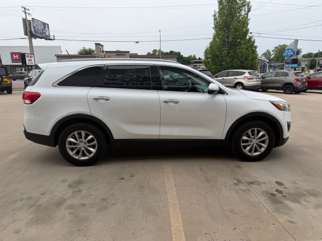 Side view of a white SUV parked in a car dealership lot with other vehicles in the background.