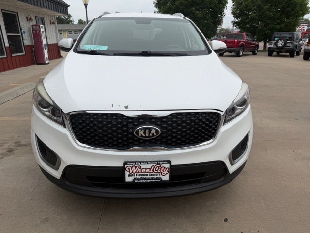Front view of a white Kia SUV parked in a car dealership lot with Wheel City Auto Finance Centers license plate frame on the bumper.