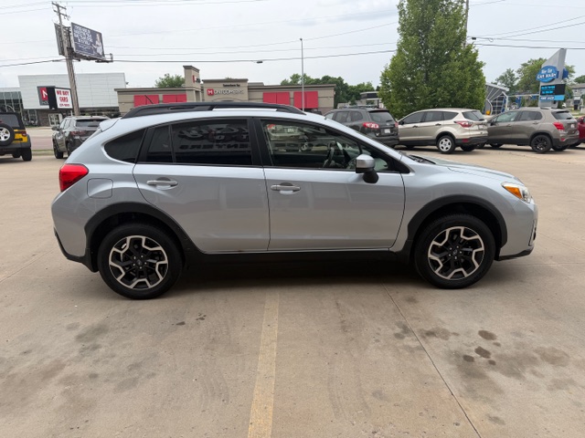 Side view of a silver crossover SUV parked in a lot, showing black alloy wheels and roof rails with other cars in the background