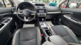 Interior view of a Subaru car: steering wheel, center console, and front seats visible from the back seat area.",