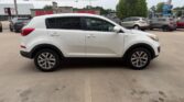 Side view of a white compact SUV parked in a dealership lot with other cars and a building in the background.