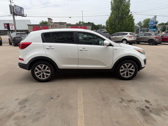 Side view of a white compact SUV parked in a dealership lot with other cars and a building in the background.