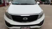 Front view of a white Kia SUV in a dealership lot, with a black honeycomb grille and Kia emblem at center, license plate frame reading Wheel City Auto Finance Centers.
