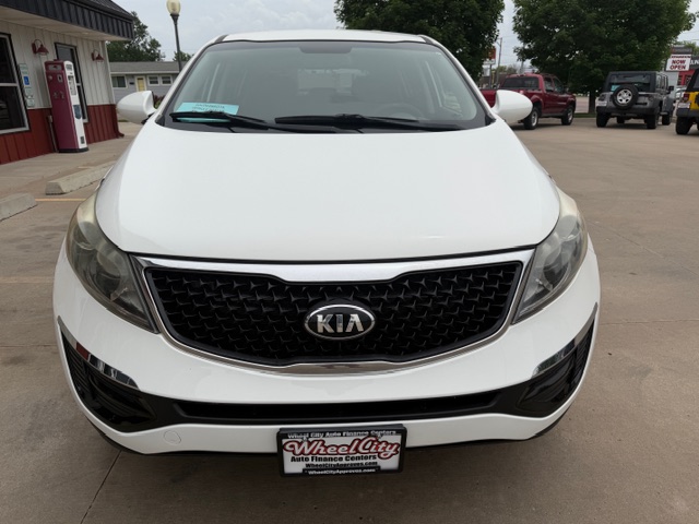 Front view of a white Kia SUV in a dealership lot, with a black honeycomb grille and Kia emblem at center, license plate frame reading Wheel City Auto Finance Centers.