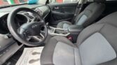 Front interior of a Kia car showing the steering wheel, dashboard with center console, gear shifter, and two-tone fabric seats; floor mat visible.