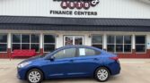 Blue sedan parked in front of Wheel City Auto Finance Centers storefront with a red bench nearby.