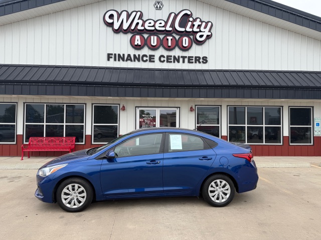 Blue sedan parked in front of Wheel City Auto Finance Centers storefront with a red bench nearby.