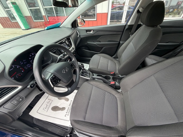 Front interior of a Hyundai car showing the steering wheel, dashboard, center console, and gray fabric seats.